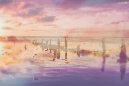 Beautiful tender sunset on the lake with stones, wooden posts and reflection, natural seasonal summer vacation backgroundの写真素材