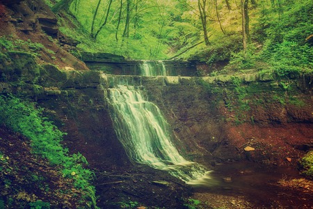 Beautiful mountain rainforest waterfall with fast flowing water and rocks, long exposure. Natural seasonal travel outdoor background in hipster vintage styleの写真素材