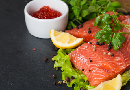 Fresh salmon with lemon, parsley, pepper and red caviar on black plateの写真素材