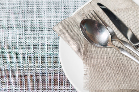 Empty white plate spoon, fork, knife on sackcloth background