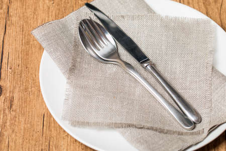 Empty white plate spoon, fork, knife on sackcloth backgroundの写真素材