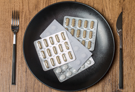 Variety of  pills on plate with fork and knife on wooden backgroundの写真素材