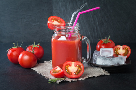 Fresh tomatoes and a glass full of tomato juice on black backgroundの写真素材