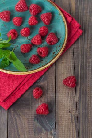 raspberries and mint leaves in a plate on wooden background