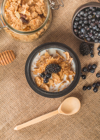 cereal flakes with fresh berries, honey and milk for breakfast on rustic backgroundの写真素材