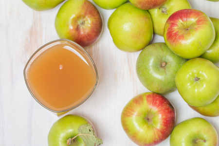 Glass of apple juice and green apples on white wooden background. Top view.