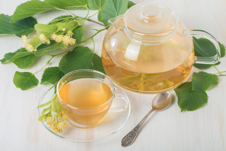 teapot and cup with linden tea and flowers on white backgroundの写真素材