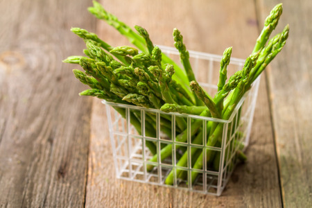 Green fresh asparagus in a plastic basket on wooden background. Selective focusの写真素材