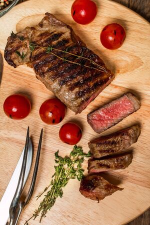 Sliced medium rare grilled Beef steak Ribeye with cherry tomatoes on cutting board on wooden background,  top viewの写真素材