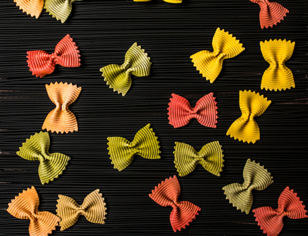 Black raw long spaghetti with colorful farfalle on wooden background. Thin pasta arranged in rows. Raw spaghetti bolognese. Food background concept. Top view.の写真素材