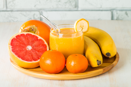 Fresh made yellow smoothie with banana, grapefruit, tangerine, persimmon on white backgroundの写真素材