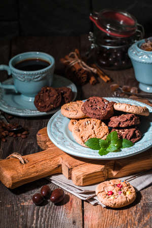 Chocolate chip cookies on plate with coffee on dark wooden table.