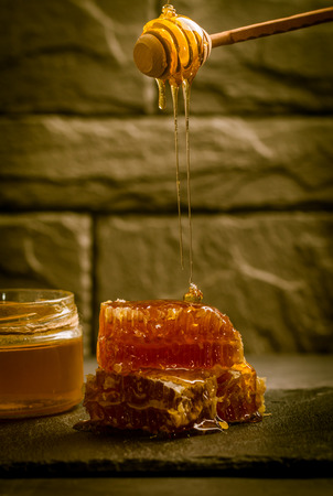 Honey dripping from a wooden honey dipper on the honeycomb on dark background