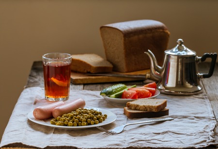 Canned green peas and sausage on the white plate with bread and tea  on linen tablecloth backgroundの写真素材