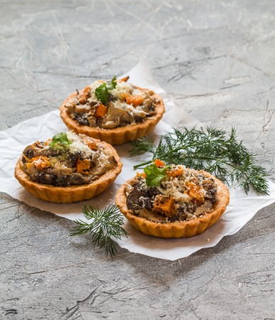 Homemade savory autumn tarts with fresh seasonal mushrooms in a crisp pastry base on gray backgroundの写真素材