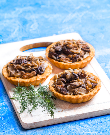 Homemade savory autumn tarts with fresh seasonal mushrooms in a crisp pastry base on blue backgroundの写真素材