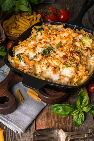 Baked pasta with broccoli, cauliflower, cheese and bechamel sauce in a frying pan on wooden backgroundの写真素材