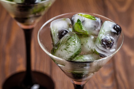 Ice cubes with dill, estragon and blueberry in glasses, on wooden backgroundの写真素材