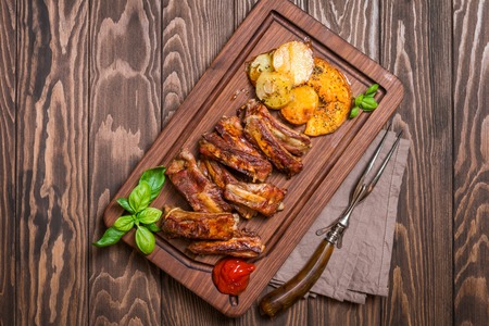 elicious Grilled Pork Rib and Fried Potato Wedges with Sauce on wooden cutting board, top viewの写真素材