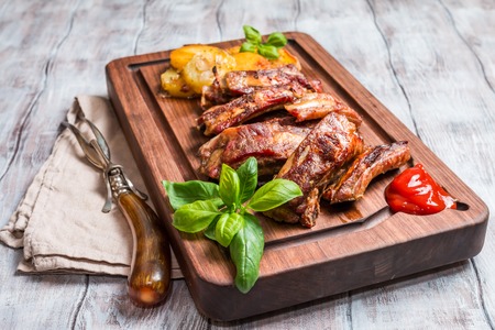 elicious Grilled Pork Rib and Fried Potato Wedges with Sauce on wooden cutting board, white wooden backgroundの写真素材