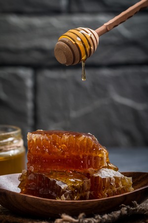 Honey dripping from a wooden honey dipper on the honeycomb on dark backgroundの写真素材