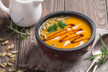 Roasted pumpkin soup with balsamic and pumpkin seeds on wooden background, close upの写真素材