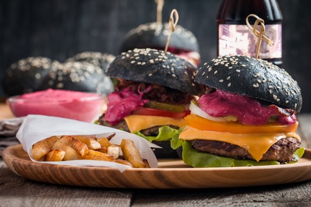 Gourmet black burger with berry sauce, french fries and drink on wooden table and dark backgroundの写真素材
