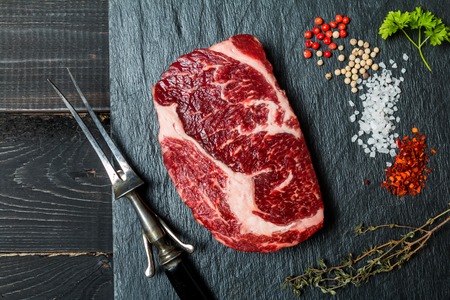 Raw fresh meat ribeye steak, chili pepper, salt and thyme on slate with meat fork on dark wooden background, top viewの写真素材