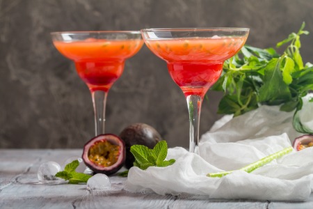 Alcoholic cocktail with fresh passion fruit, mint and ice on gray background.の写真素材