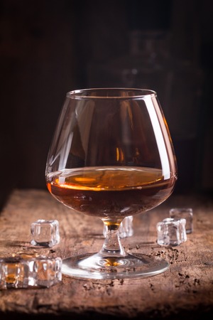 Glass of brandy or cognac on old oak wooden table. Dark photo.の写真素材