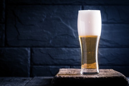 Glass of light beer with bubbles near black wallの写真素材
