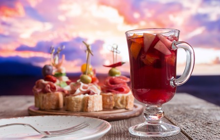 Set of Spanish tapas served on a sliced baguette with sangria on wooden table against the seaの写真素材