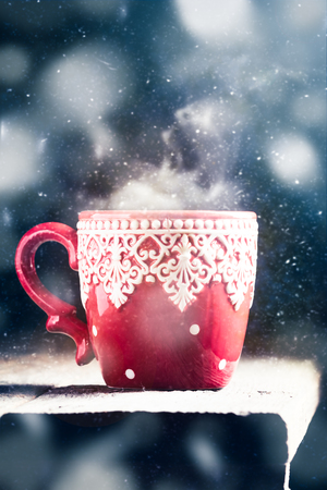 Red winter cup with hot drink on table with snowy christmas backgroundの写真素材