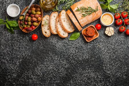 Italian fresh ciabatta bread cut in slices with herbs, garlic, sun-dried tomatoes and olives over...