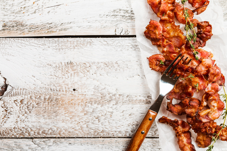 Fried bacon with sauce and greens on paper over old white wooden background. Top viewの写真素材