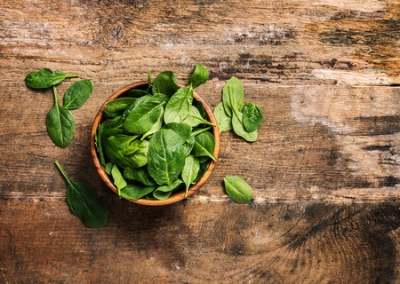 bunch of fresh spinach leaves in a bowl on wooden background, top view with copy spaceの写真素材