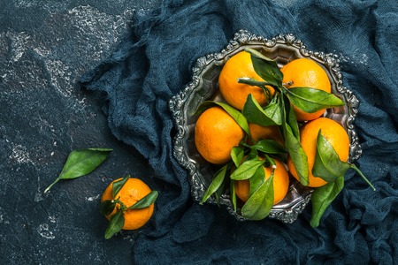 Fresh tangerines with leaves in metal bowl on dark background. Top view with copy space.の写真素材