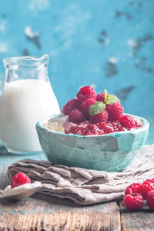 Fresh homemade cottage cheese with juicy raspberries on rustic wooden table, dietary breakfast for summer timeの写真素材