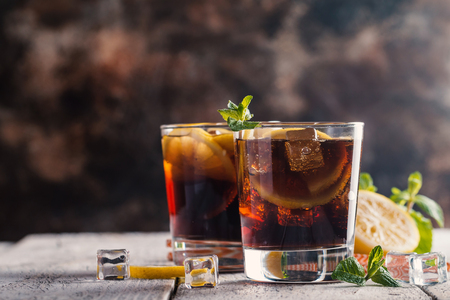 Fresh made Cuba Libre with brown rum, cola, mint and lemon on wooden backgroundの写真素材