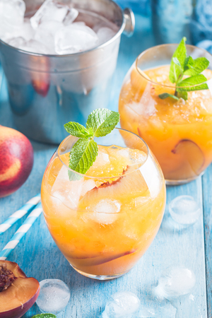 Peach cocktail or tea with ice and mint on blue background.の写真素材