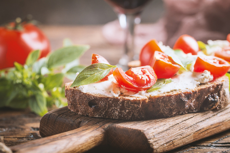 Close up of crostini appetizers with cherry tomatoes, basil, and cheese on cutting boardの写真素材