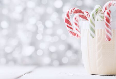 A knitted print cup with Christmas candies in front of white bokeh backgroundの写真素材