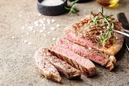 Sliced medium rare grilled beef steak with rosemary and spices on dark rustic background, top view, place for textの写真素材