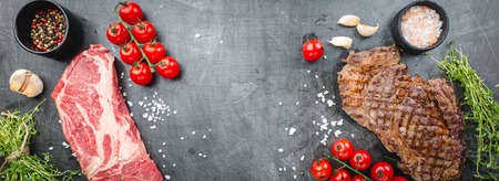 Grilled and raw ribeye beef steaks with herbs and spices for cooking over black background. Top viewの写真素材