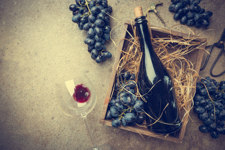 A bottle of red wine in a box with grapes on a gray stone background, copy space , top view.の写真素材