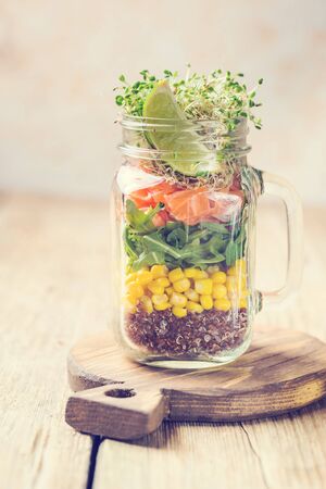 Fresh spring salad with salmon, quinoa, arugula, cress salad and corn in a mason jar for a snack with you. The concept of healthy proper nutrition.の写真素材