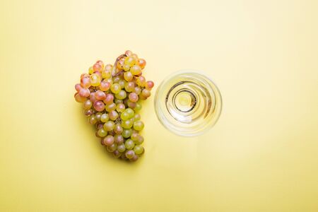 Glass of white wine and ripe grapes on yellow background, top viewの写真素材