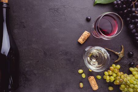 Glasses of white and red wine with ripe grapes on black stone background, top view