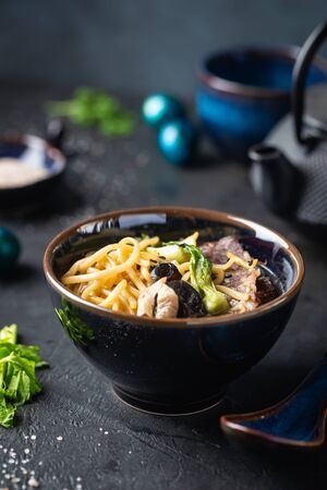 Asian ramen noodles soup with beef, oyster mushrooms and vegetables in bowl on dark backgroundの写真素材