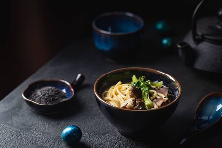 Asian ramen noodles soup with beef, oyster mushrooms and vegetables in bowl on dark background